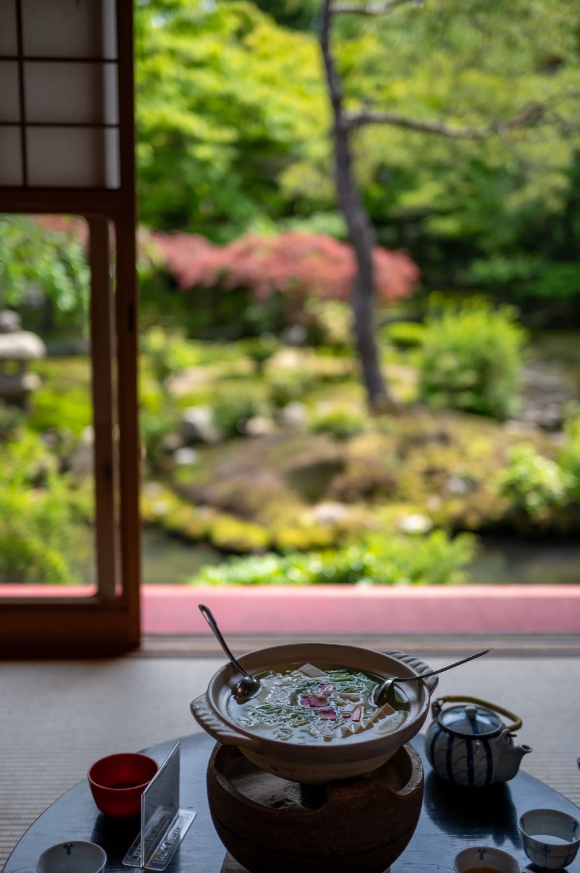 A pot simmering on a low table in a tatami room, the sliding screen open onto a moss garden